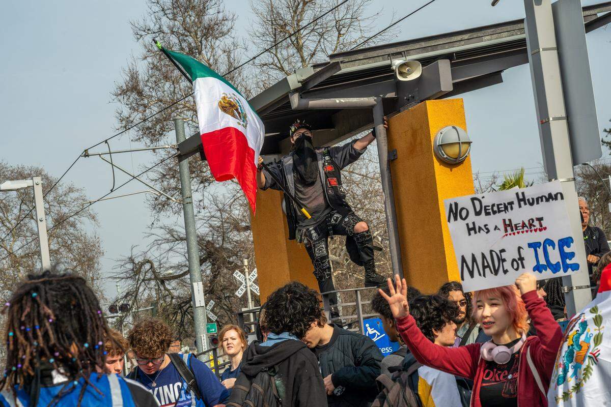Jackson Destefano, at right, waves and holds a sign alongside McClatchy High students catching light rail during a districtwide walkout on Friday in Sacramento, part of a nationwide student effort to protest immigration enforcement following fatal shootings in Minneapolis.