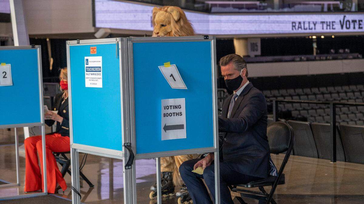 California Gov. Gavin Newsom, right, and First Partner Jennifer Siebel Newsom, left, vote in socially distanced booths under the watchful eye of the Sacramento Kings mascot Slamson the Lion, at Golden 1 Center in Sacramento on Thursday, Oct. 29, 2020.