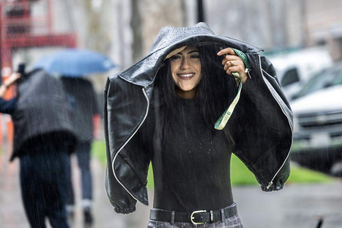 Azaria Loya, of Sacramento, covers herself from the rain on Friday, March 1, 2024, on 22nd Street in midtown Sacramento.