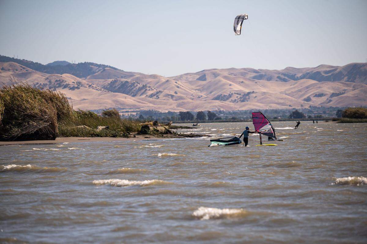 A man prepares to wing foil while others windsurf and kiteboard at Sherman Island County Park on May 13, at the south end of Sacramento County. On hot summer days, the Delta breeze benefits wind-sports enthusiasts, the Montezuma Hills wind turbines in Solano County, as well as Sacramento residents.