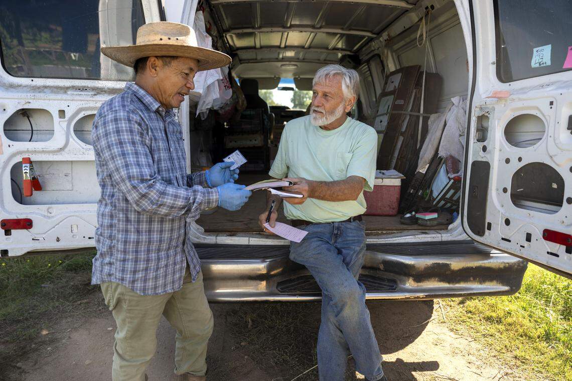 Marysville farmer James Thao gets a check earlier this month from Steven Dambeck, who works as an aggregator for the Farms Together program, a federally funded state effort that helps small farms sell their produce to local food banks.