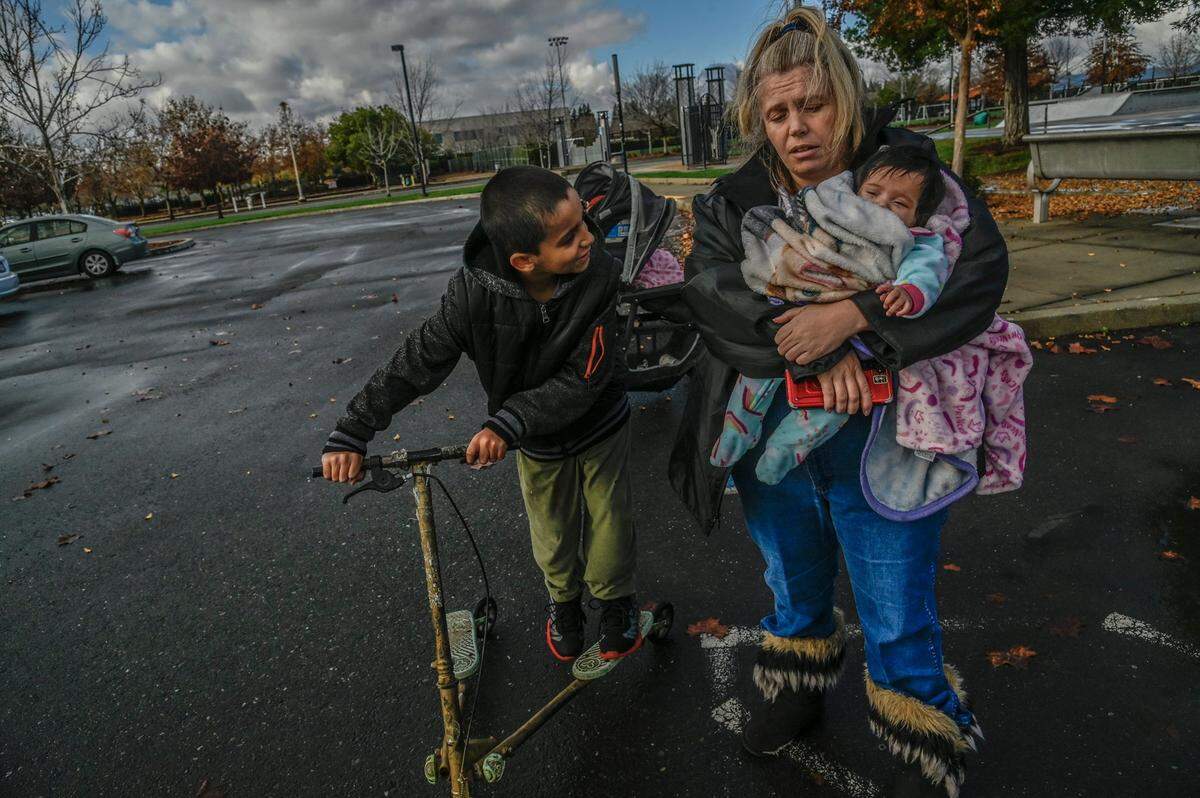 Geri Wells, 36, holds 3-month-old daughter Orion while her son Gabriel Gonzales, 9, gets ready to play on his scooter at a park in Rancho Cordova on Thursday, Dec. 9, 2021. The homeless family had their motorhome towed last month by the city and is now living in their SUV. As she approached the tow truck that day, Wells said she was yelling You cant take my home, this belongs to my children! This is their only place to sleep! What are you doing?
