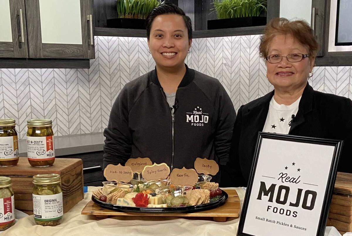 Dee Siazon and her mother Delia "Mama Mojo" Siazon showcase Real Mojo Foods pickles alongside crackers, cheese and fruit as part of a platter. The Hot-n-Zesty Semi-Sweet & Spicy pickle chips are a finalist in the 2026 Good Food Awards.