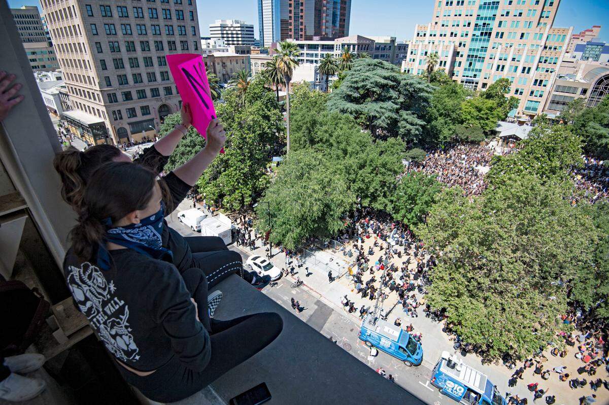Protesters sit in on top of a parking garage near Caesar Chavez Plaza in Sacramento, Saturday, June 6, 2020, looking over a large crowd gathered to protest the killing of George Floyd that had marched from Golden 1 Center.