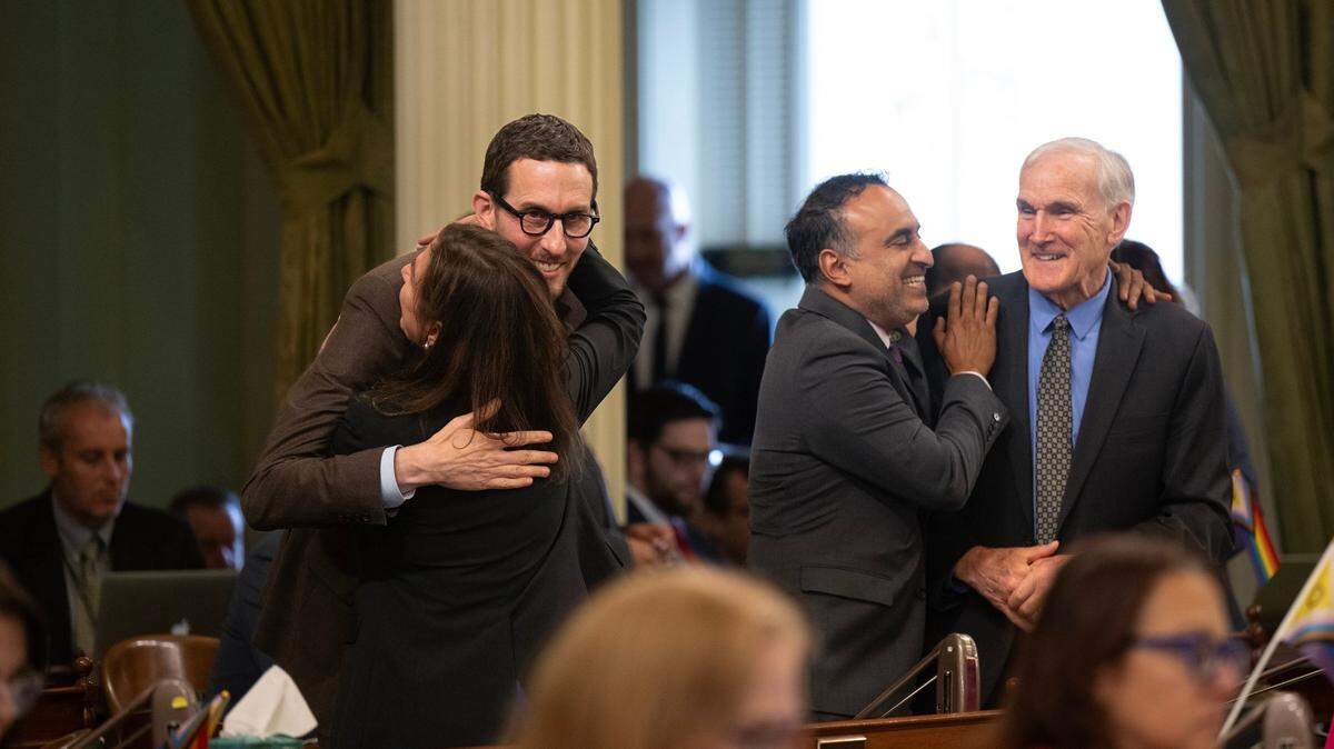 State Sen. Scott Wiener, D-San Francisco, and Assemblywoman Diane Papan, D-San Mateo, embrace at left while Assemblymen Ash Kalra, D-Santa Clara, and Steve Bennett, D-Ventura, hug at right following a vote Wednesday on SB 1047, a bill that intends to regulate artificial intelligence.