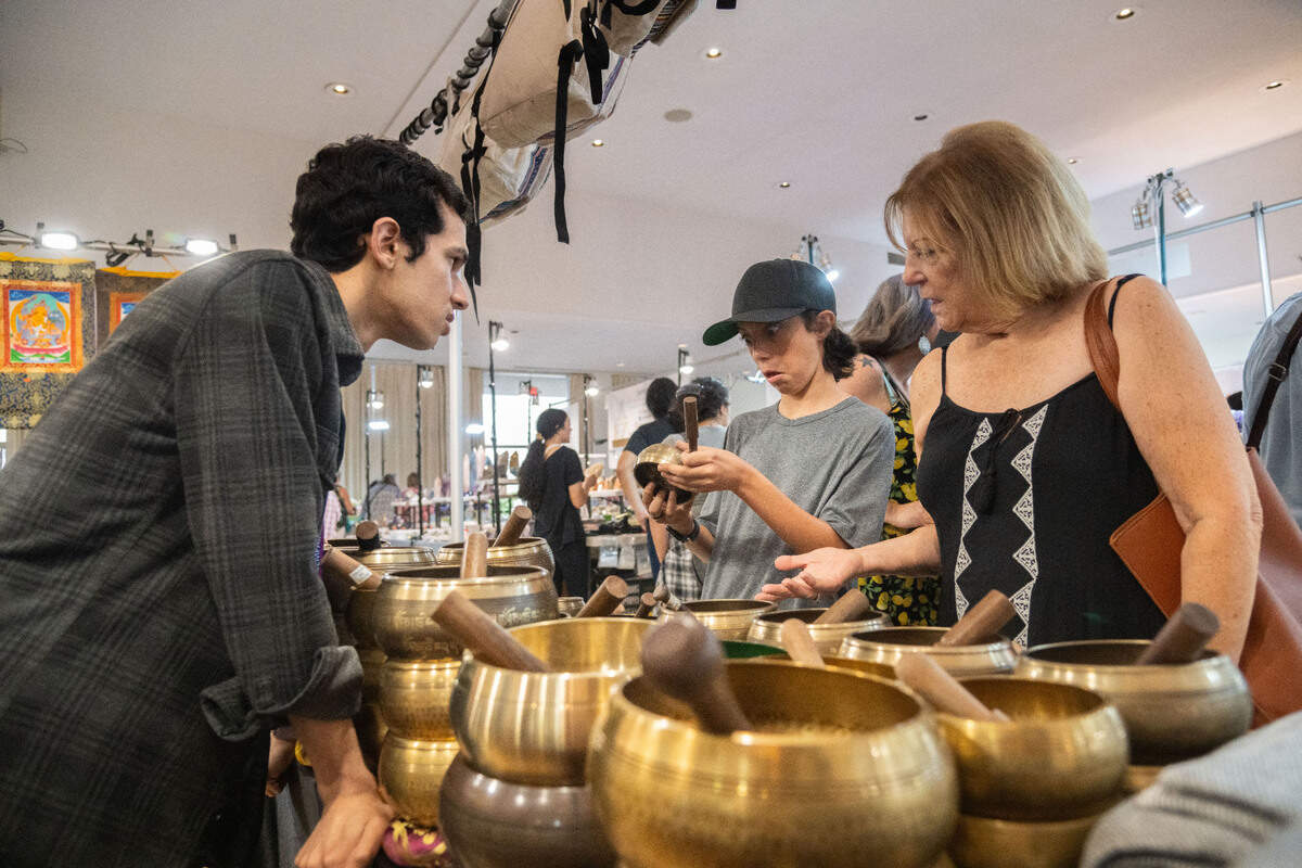 Roshan Thapaliya, left, explains how song bowls’ pitches work to Connor Young, 12, center, and Sandy Patitucci, right, at Navadurga Handicrafts’s booth during the Gem Faire at the Scottish Rite Masonic Center in Sacramento on Friday, Aug. 2, 2024. “This was the deepest beginner one,” Young said of the song bowl his grandmother, Patitucci, bought him.