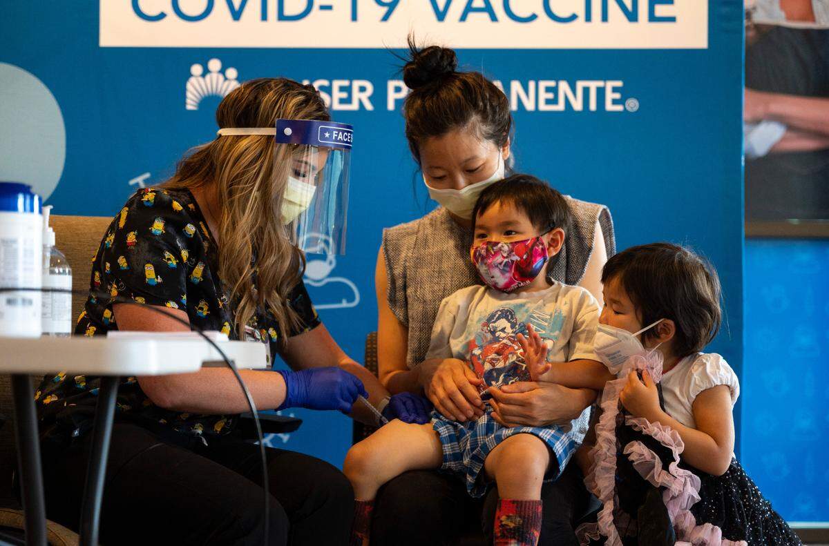 Colton, 3, receives a Pfizer COVID-19 vaccination from nurse Samantha Abadilla while being held by mother Kimberly Truong and watched by just-vaccinated twin sister Brie at the Kaiser Permanente Bruceville Center Vaccination Clinic in Sacramento on Thursday, June 23, 2022. Children ages six months to five years began receiving the inoculations at the clinic on Wednesday, after the recent recommendation by the Centers for Disease Control.
