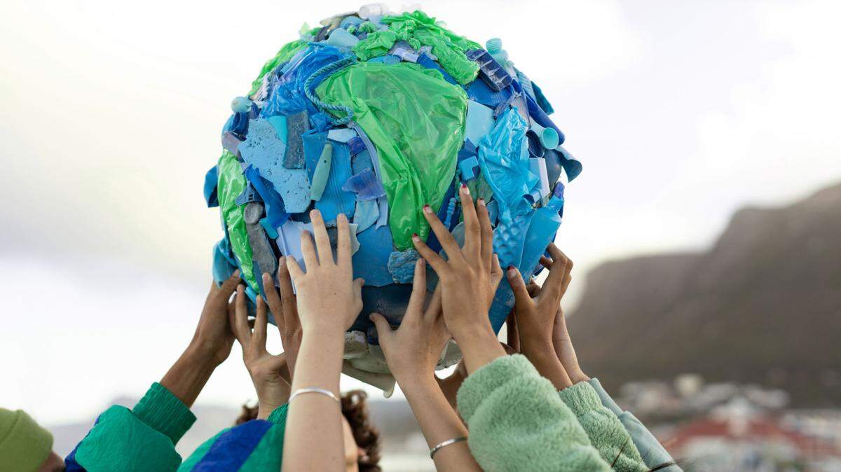 Friends hold up a sculpture depicting the world made from plastic pollution collected on beaches.