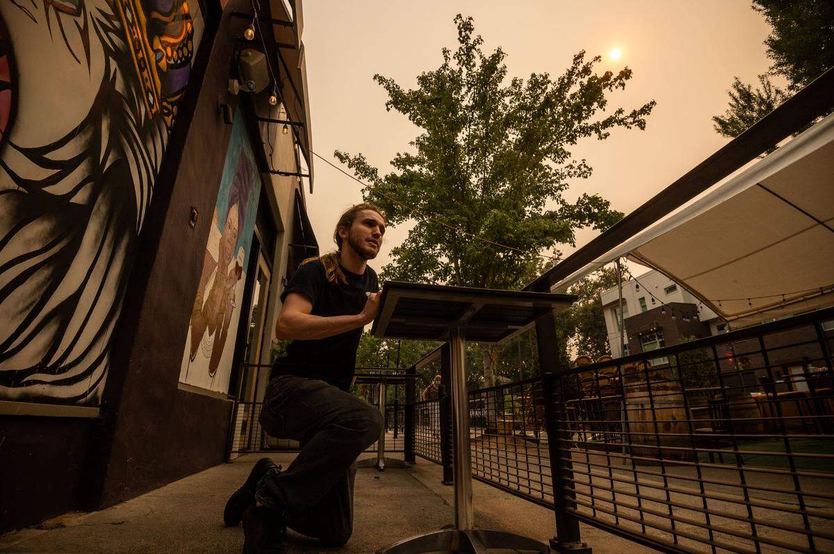 Garrett Barcus, of Roseville, sets up tables outside of a Handle District restaurant and lounge 58 Degrees & Holding Co, on 18th Street near other outside dining areas in midtown Sacramento on Wednesday. Smoke from fires across the northern state, including the Caldor Fire in El Dorado County, was tinting the sky and lowering air quality.