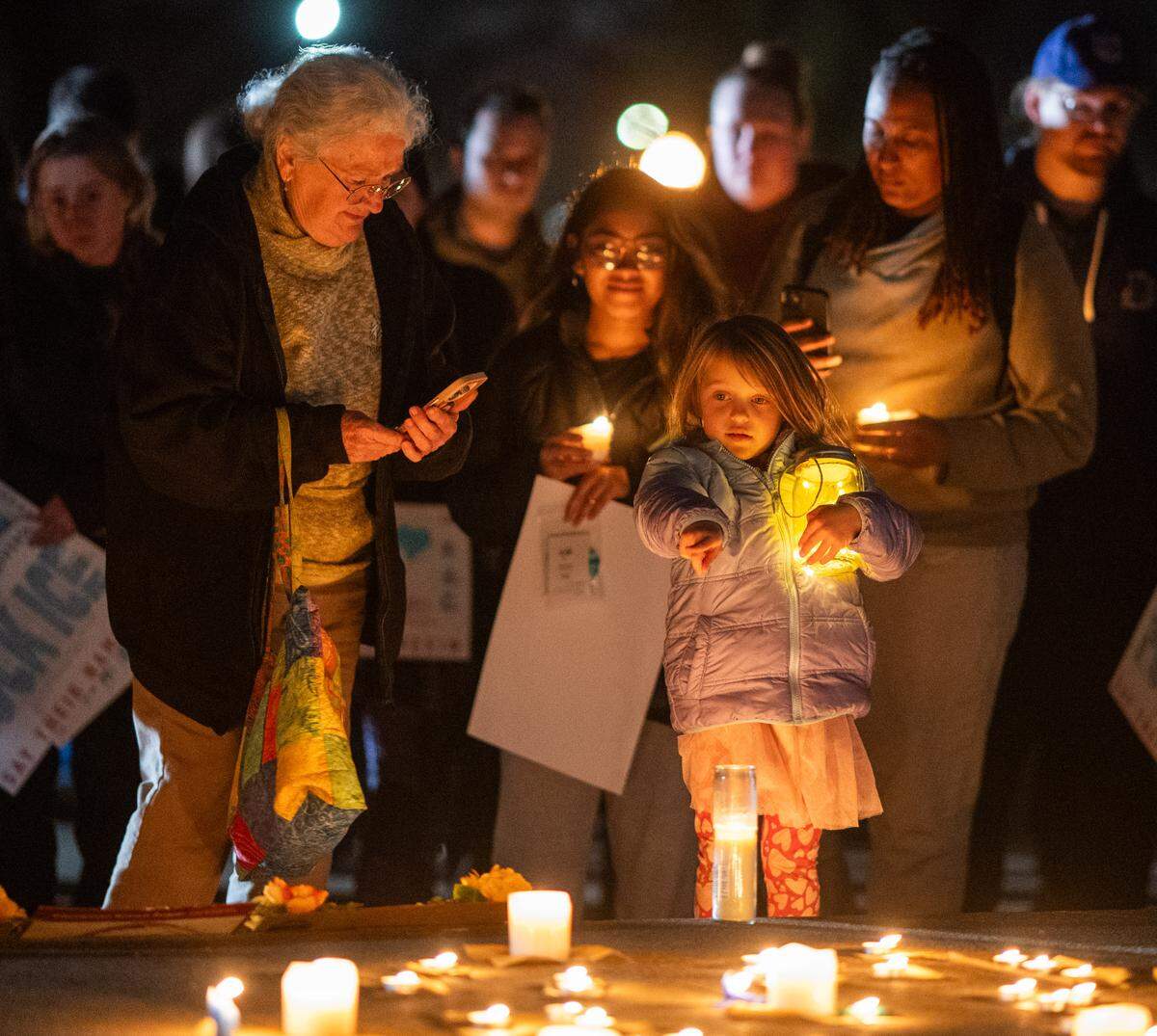 Ava Beauton points to candles on a memorial to people killed by ICE as her great aunt Catherine Hourcade prepares to take a picture during a vigil at Southside Park in Sacramento on Monday.