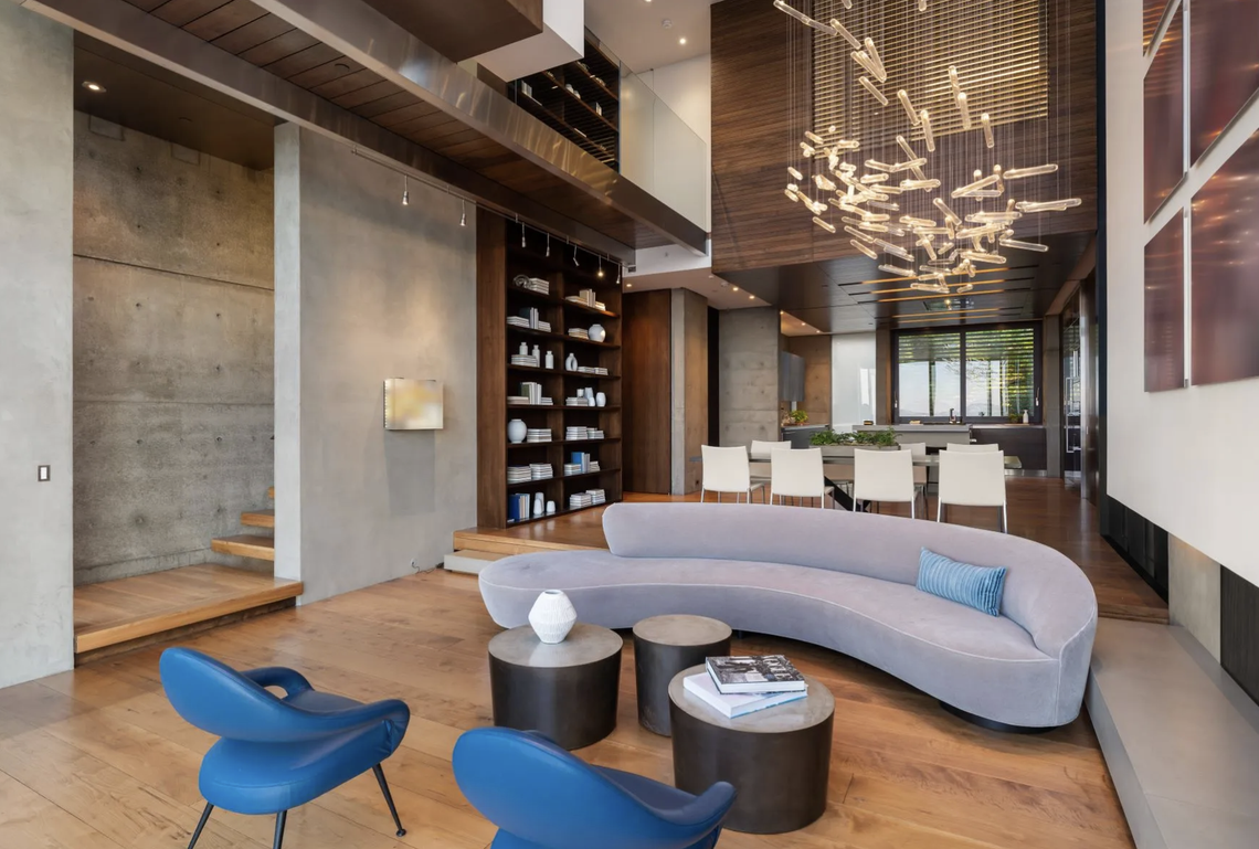 Twelve-foot pivot doors open to a cantilevered terrace, creating a sensory indoor-outdoor experience. A dramatic 13’ light sculpture floats above the dining area, while a custom walnut-accented kitchen conceals behind movable glass panels.