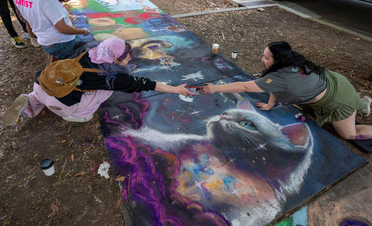 Artists Allie Nanni, left, and Lucia Colombo work together on a sidewalk mural of space cats while helping artist Susan Stewart of Strapping Store at the Chalk it Up festival on Sunday at Fremont Park.