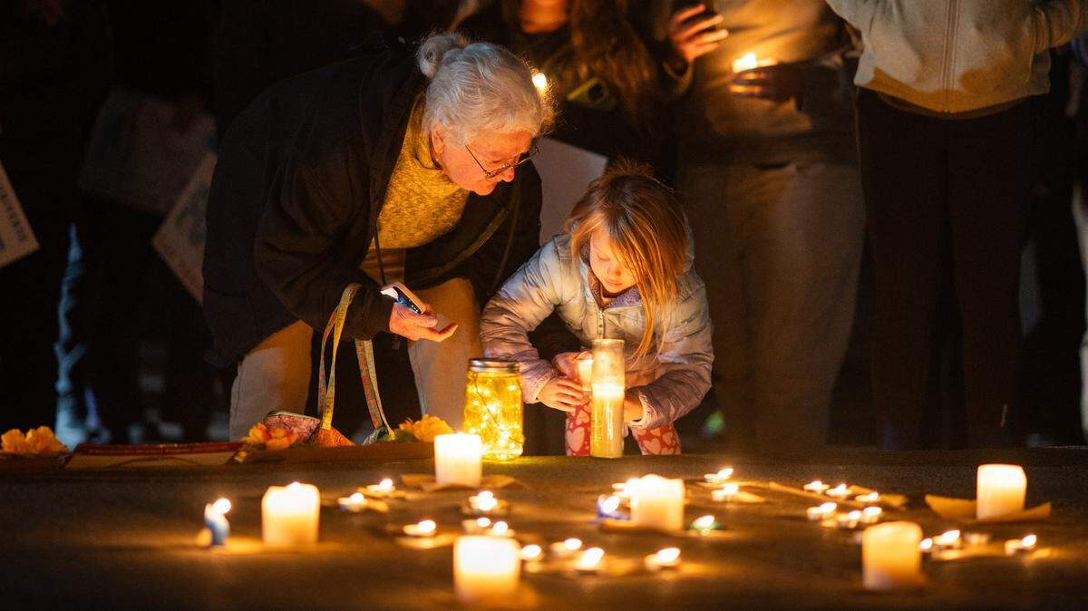 Ava Beauton, joined by great aunt Catherine Hourcade, places a candle on a memorial to people killed by ICE during a vigil at Southside Park in Sacramento on Monday.