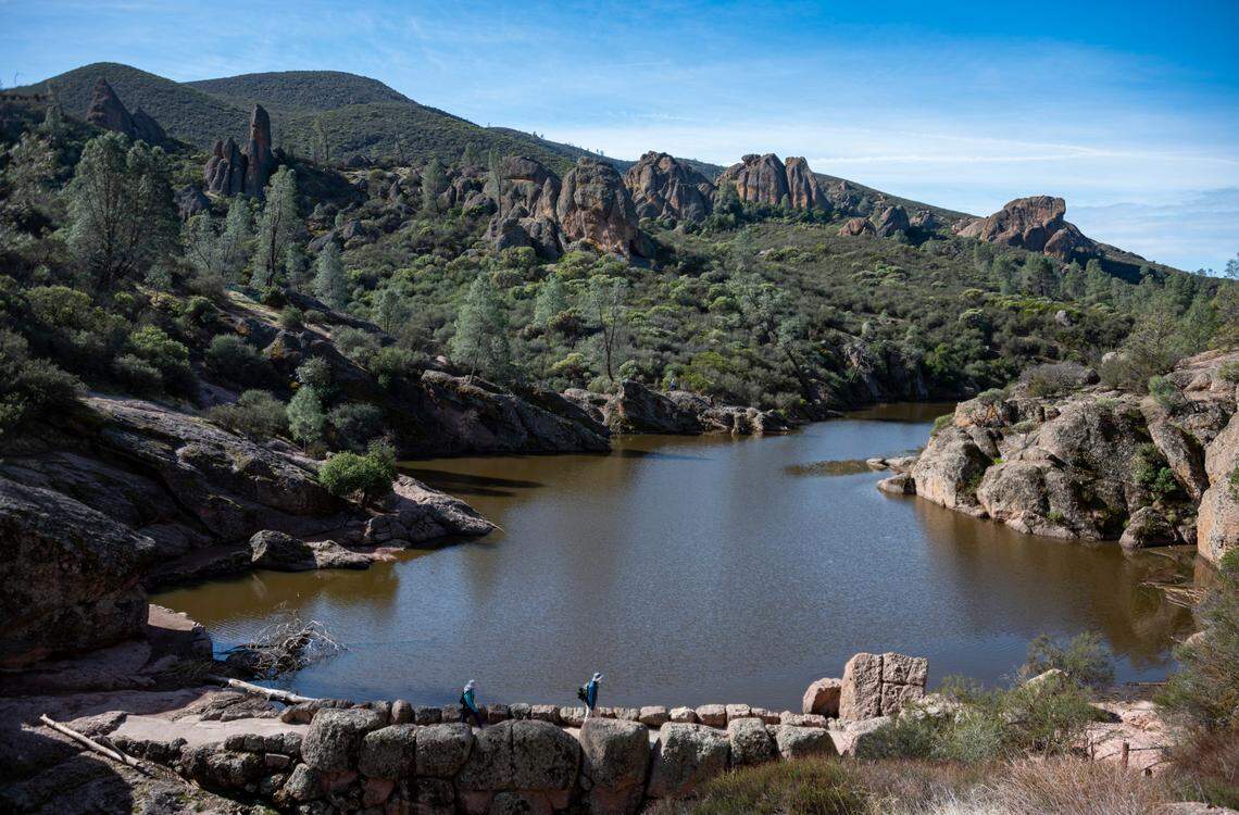 Hikers cross the Bear Gulch Reservoir dam as seen from the Rim Trail in Pinnacles National Park in Feburary 2021.