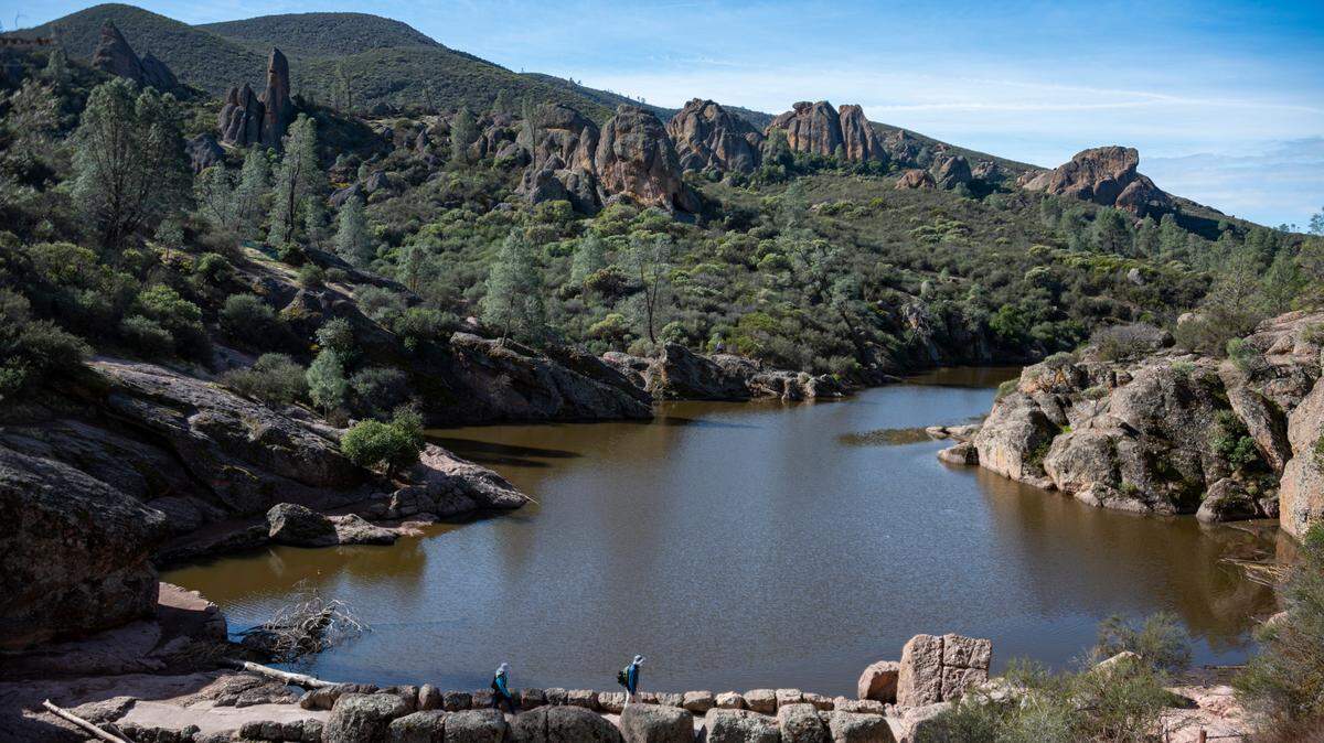 Hikers cross the Bear Gulch Reservoir dam as seen from the Rim Trail in Pinnacles National Park in Feburary 2021.