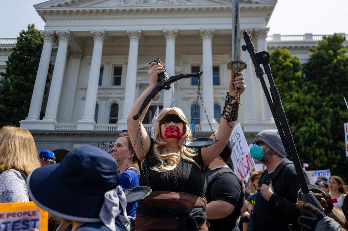 Dressed as a black-clad Lady Justice, Sacramento resident Nichole Ftacnik holds scales and a sword during the 50501 protest against the Trump administration at the state Capitol on Saturday, April 4, 2025 in Sacramento.