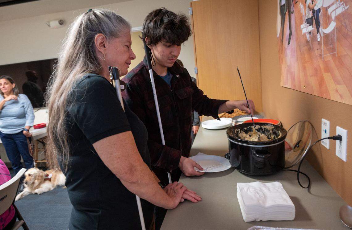 Diane Starin, a living skills instructor with Society for the Blind, helps Spencer Parod get food at their holiday potluck last month.