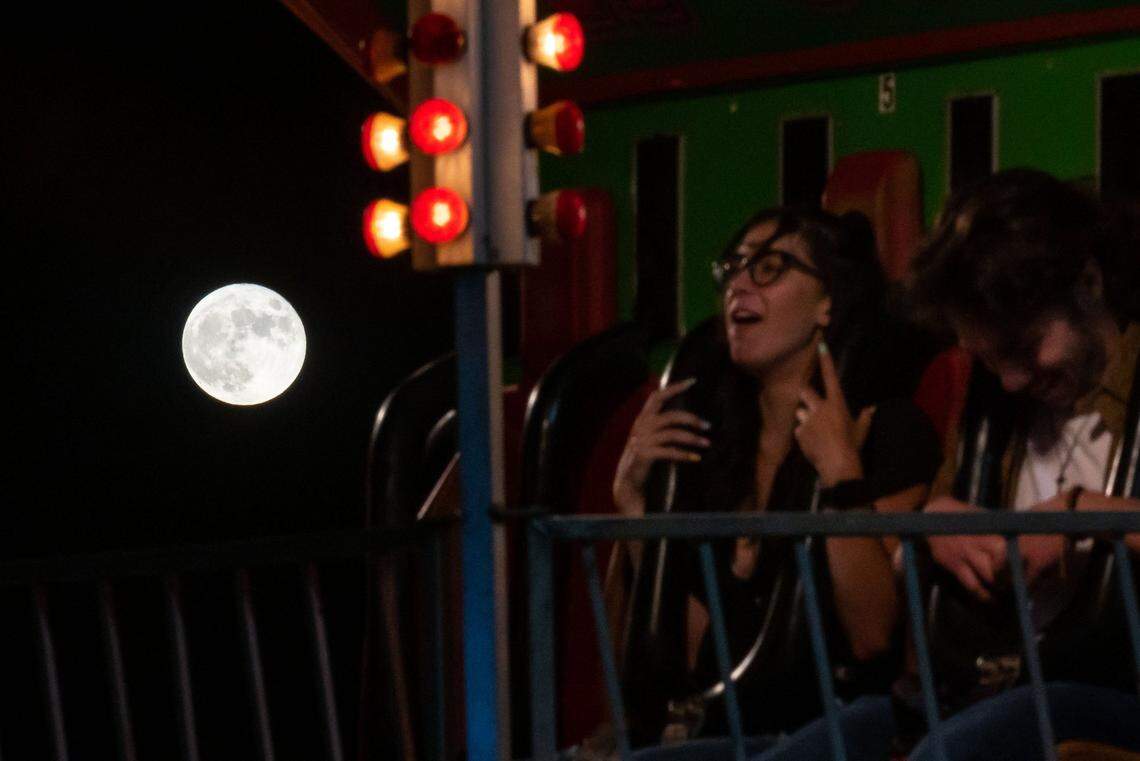 The strawberry full moon rises in the sky as Taylor Dix, left, and boyfriend Jordan Watson, both of Roseville, gather themselves after a fast drop during the Rip Cord ride at the Placer County Fair on opening night June 24, 2021, in Roseville. 
