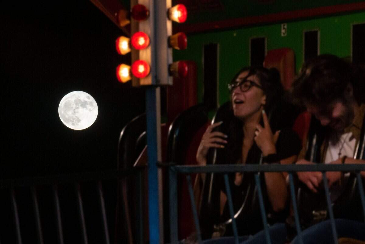 The strawberry full moon rises in the sky as Taylor Dix, left, and boyfriend Jordan Watson, both of Roseville, gather themselves after a fast drop during the Rip Cord ride at the Placer County Fair on opening night June 24, 2021, in Roseville.