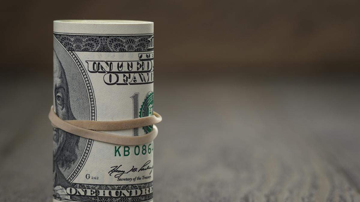 roll of old style hundred dollar bills stand on wooden table
