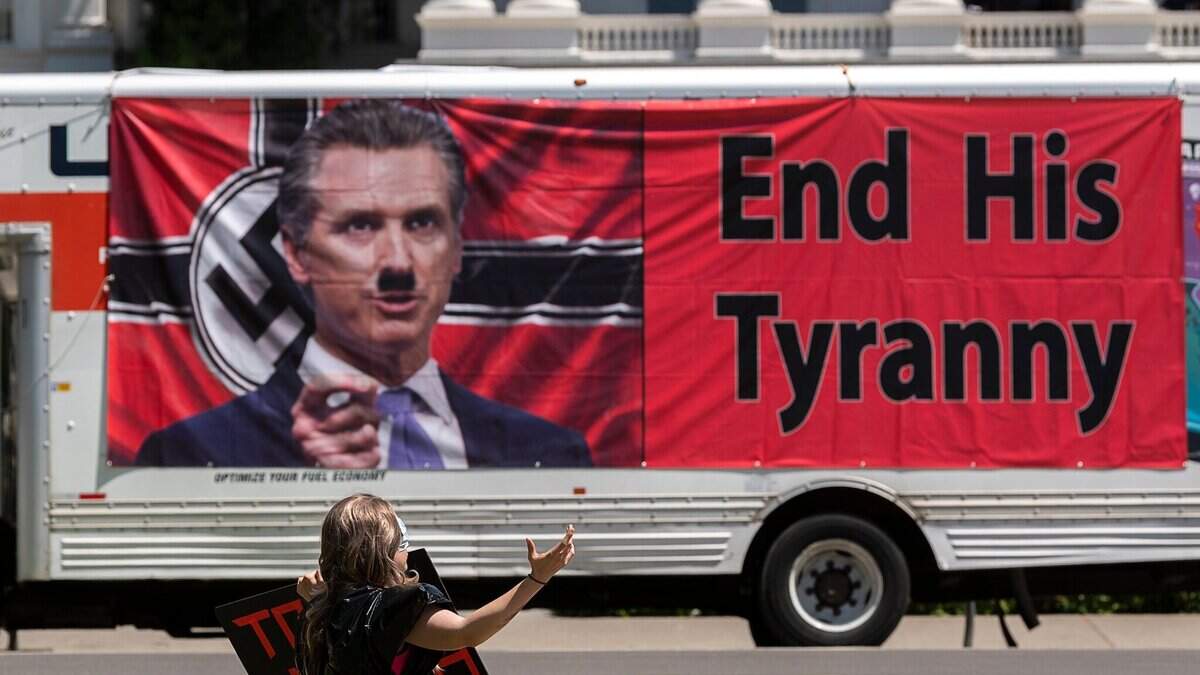 A banner at a protest against coronavirus stay-at-home orders shows Gov. Gavin Newsom on a Nazi flag with an Adolph Hitler mustache at the state Capitol on Thursday, May 7, 2020.