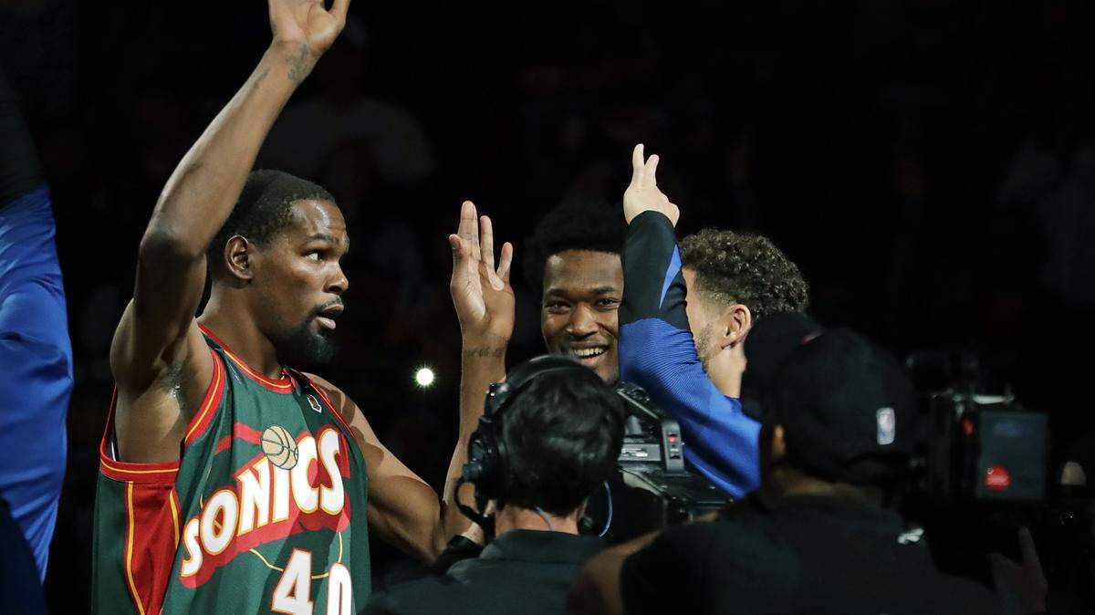 Golden State Warriors forward Kevin Durant, left, appears during player introductions wearing the jersey of Seattle SuperSonics great Shawn Kemp as he greets teammates before an NBA basketball preseason game against the Sacramento Kings, Friday, Oct. 5, 2018, in Seattle.