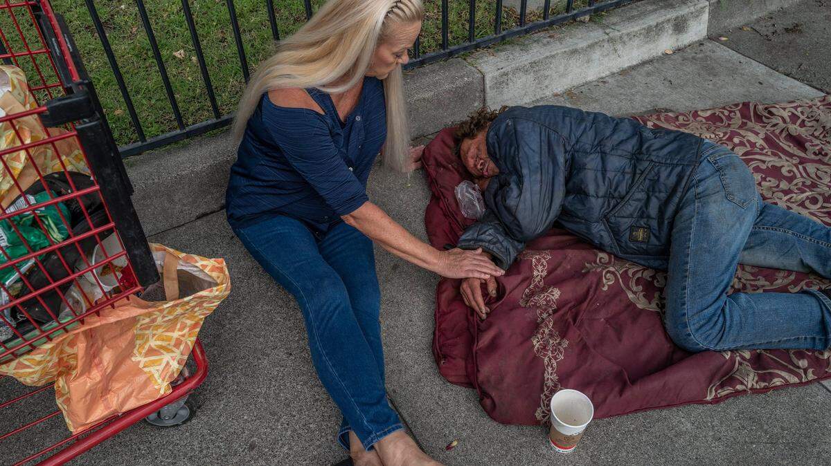 Linda Privatte, 65, caresses her brother Mark Rippee’s hand as she gently tries to wake him up on a sidewalk in Vacaville, Monday, Aug. 1, 2022. “Is it okay for me to clean your cart out for you so I can see what you need?” she asked.