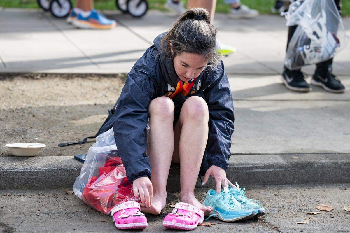Kelsey Alves, of Monterey takes off her shoes to put on Crocs after finishing the 40th California International Marathon from Folsom to the state Capitol in downtown Sacramento on Sunday, Dec. 3, 2023.