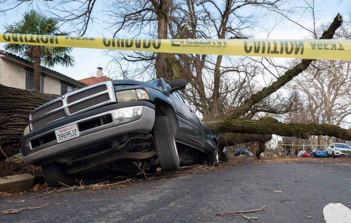 The front wheel of a truck on 24th Avenue in Curtis Park is suspended above the ground on Sunday, Jan. 8, 2022, after a tree fell across the street, crushing the back of the vehicle. A storm with high winds knocked out power to more than 300,000 residents of Sacramento County.