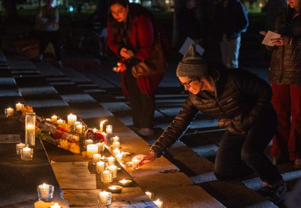 A woman places a candle on a memorial to people killed by ICE during a vigil at Southside Park in Sacramento on Monday.