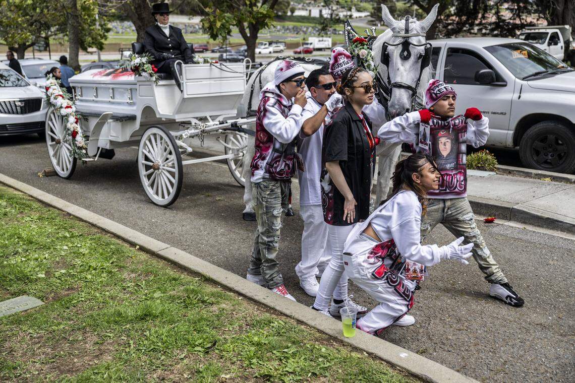 Jhanelly, the sister of Jesus and Jhony Ramos, bottom right, poses for a photo with other mourners in front of a horse-drawn carriage carrying the casket of Jesus on Monday in Greenlawn Memorial Park in Colma. 