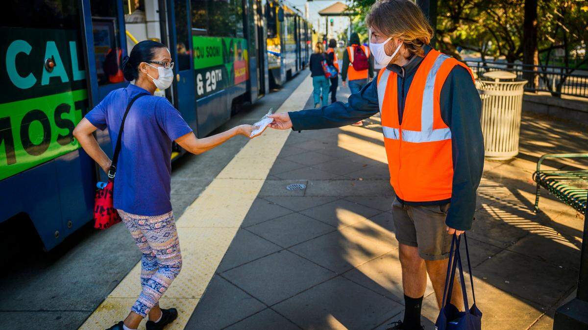 Volunteer Daniel Domich, 26, of Sacramento, right, hands a Sacramento Regional Transit mask to a passenger getting off at the 39th Street/UC Davis Health light rail stop in East Sacramento on Wednesday, July 22, 2020. SacRT received 30,000 masks from from the California Office of Emergency Services and the Federal Transit Administration. Riders are required to wear them on RT trains and buses, or while waiting at stations and stops. The masks are reusable and can be washed.