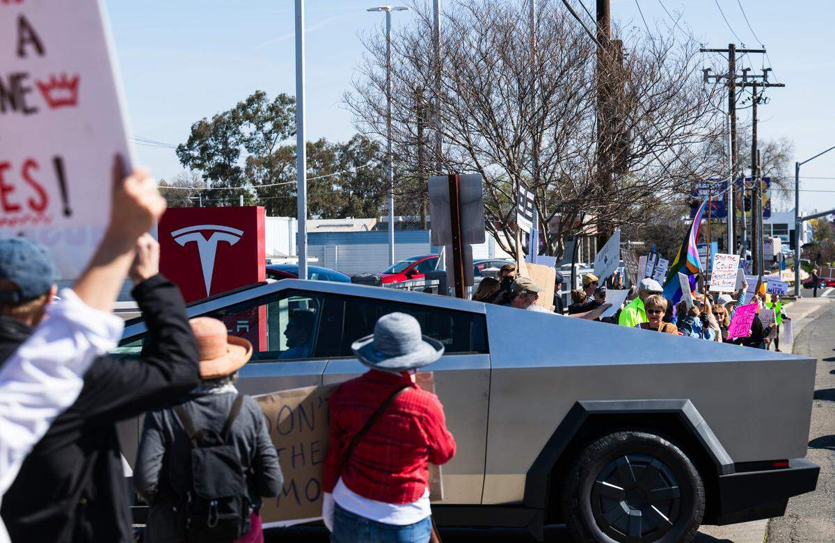 A Cybertruck drives into a Tesla dealership on Arden Way near Sacramento as demonstrators rally against Elon Musk on Saturday, March 8, 2025. More than 100 people lined both sides of street to protest the role of the tech billionaire and Tesla CEO in the Trump administration.