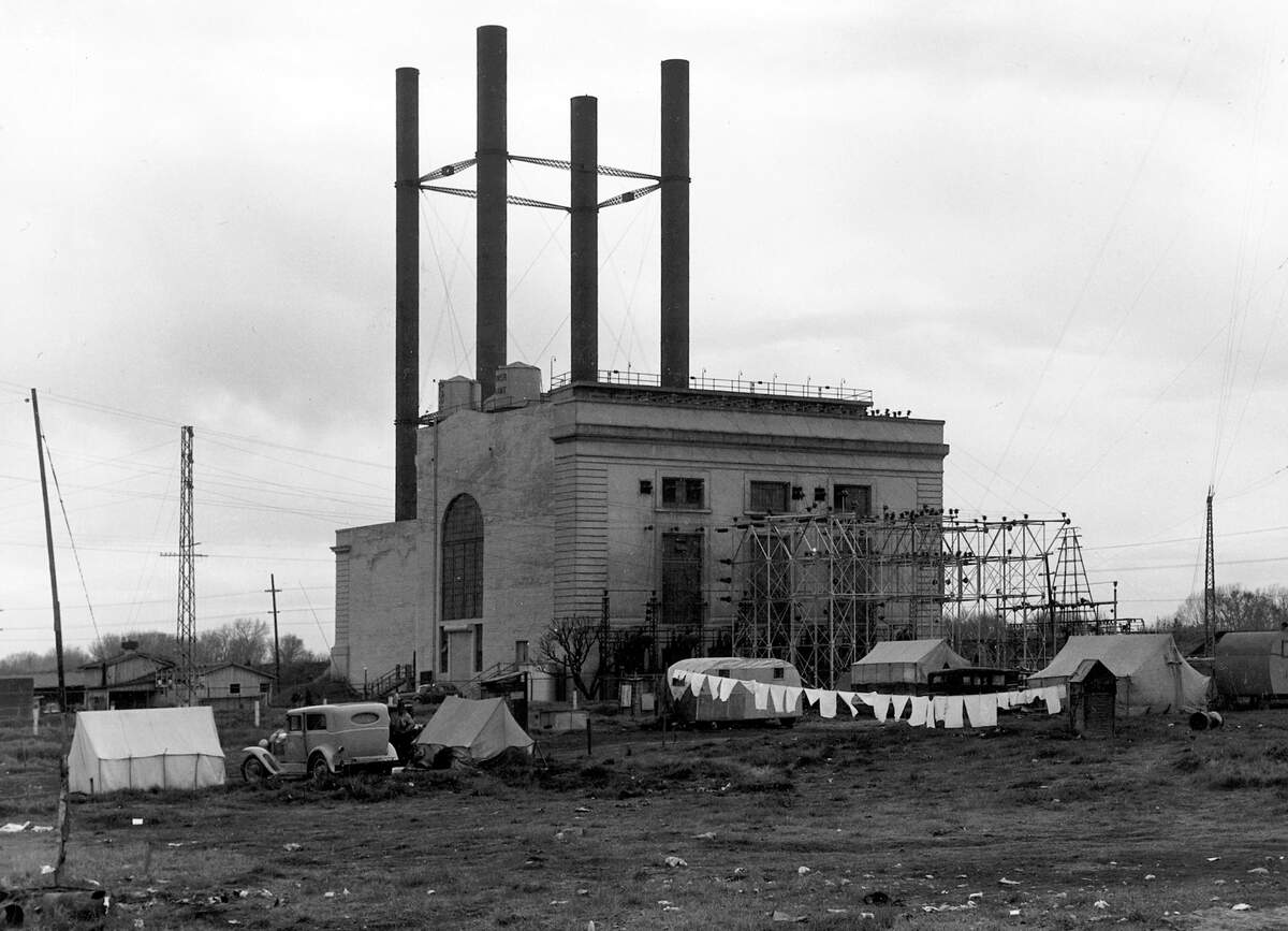 The PG&E power station, with its four dramatic smokestacks that would belch dark smoke during the operation of its oil-powered steam turbines, was only used for auxiliary and testing purposes in the 1930s and 1940s. More than 100 farmworker families were camping nearby without sanitary facilities when famed photographer Dorothea Lange visited the location in 1940.