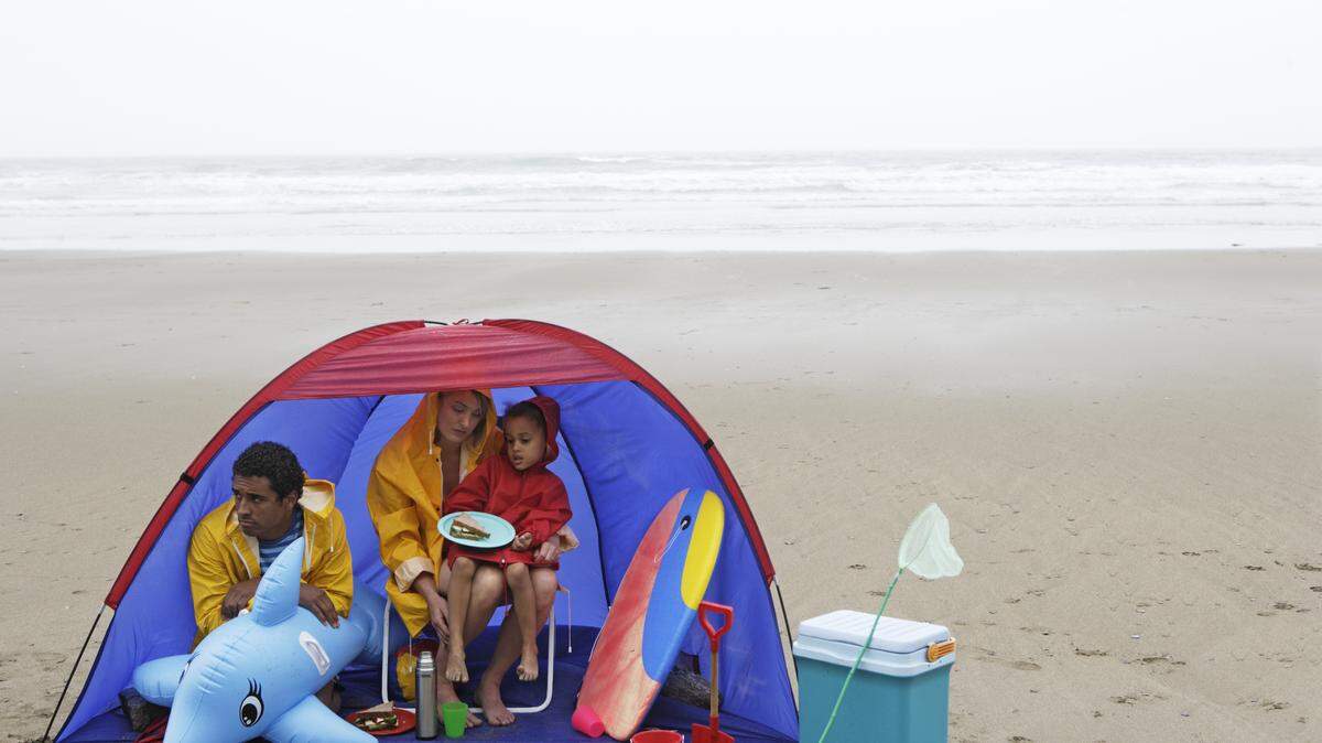 Family looking disappointed on the beach in the rain. 