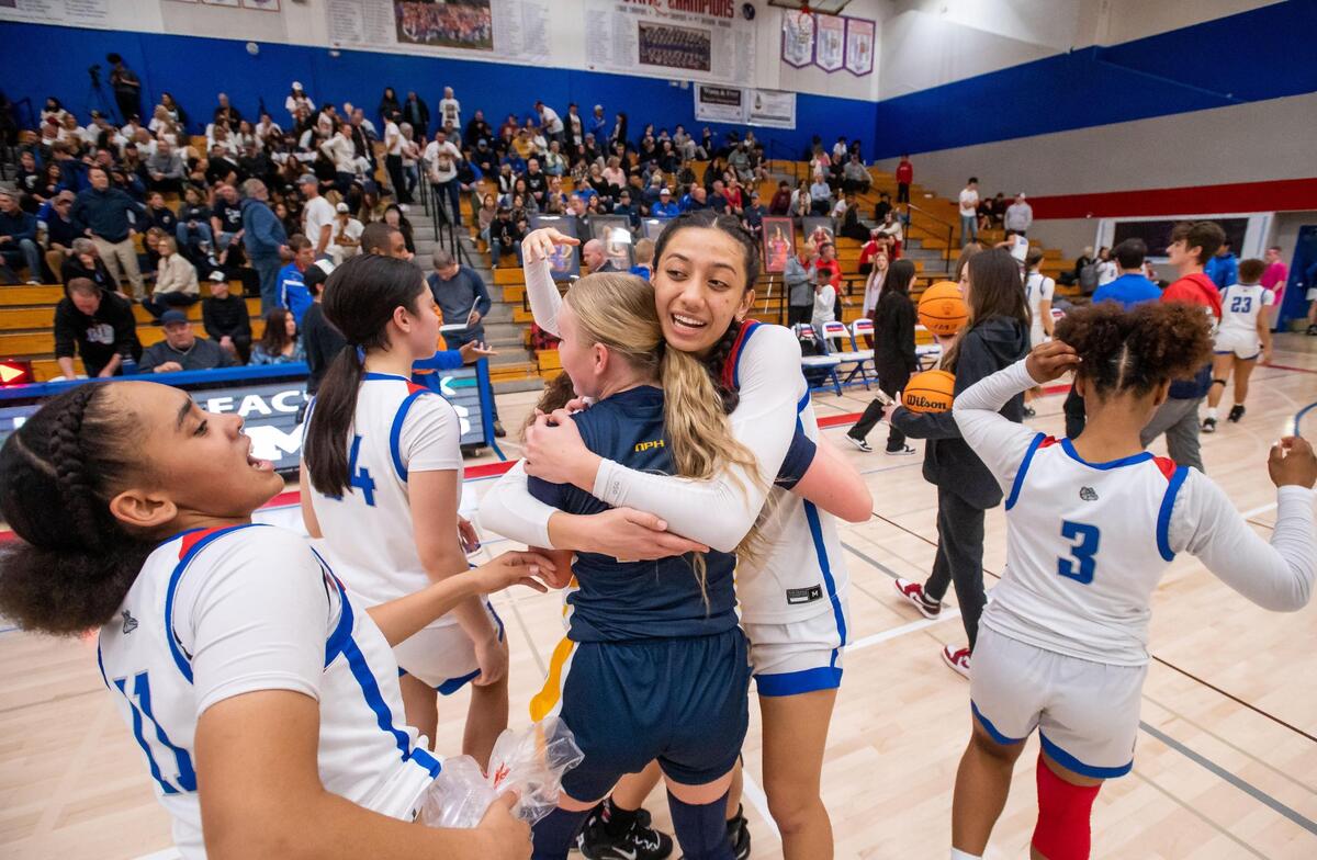 Folsom Bulldog Kamryn Mafua (14), center, embraces Oak Ridge Trojan Ava Edwards (14) as they congratulate each other on a well-played rivalry high school girls basketball Sierra Foothill League game Friday, Feb. 10, 2023, at Folsom High School. Folsom Bulldog guard Aryn Bright (11) ices her hip at left after the Bulldogs defeated the Trojans 64-35 on senior night.