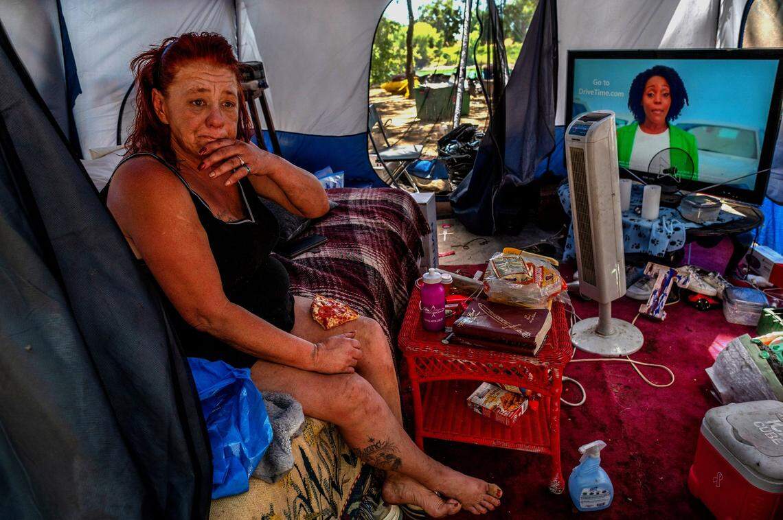 Twana James, 53, rests in her tent with a piece of pizza on her lap given to her by a neighbor on July 6, at their homeless camp along the Sacramento River near Discovery Park. She said most of the furniture and the TV were found in a dumpster. “They throw away the darnedest things,” she said.