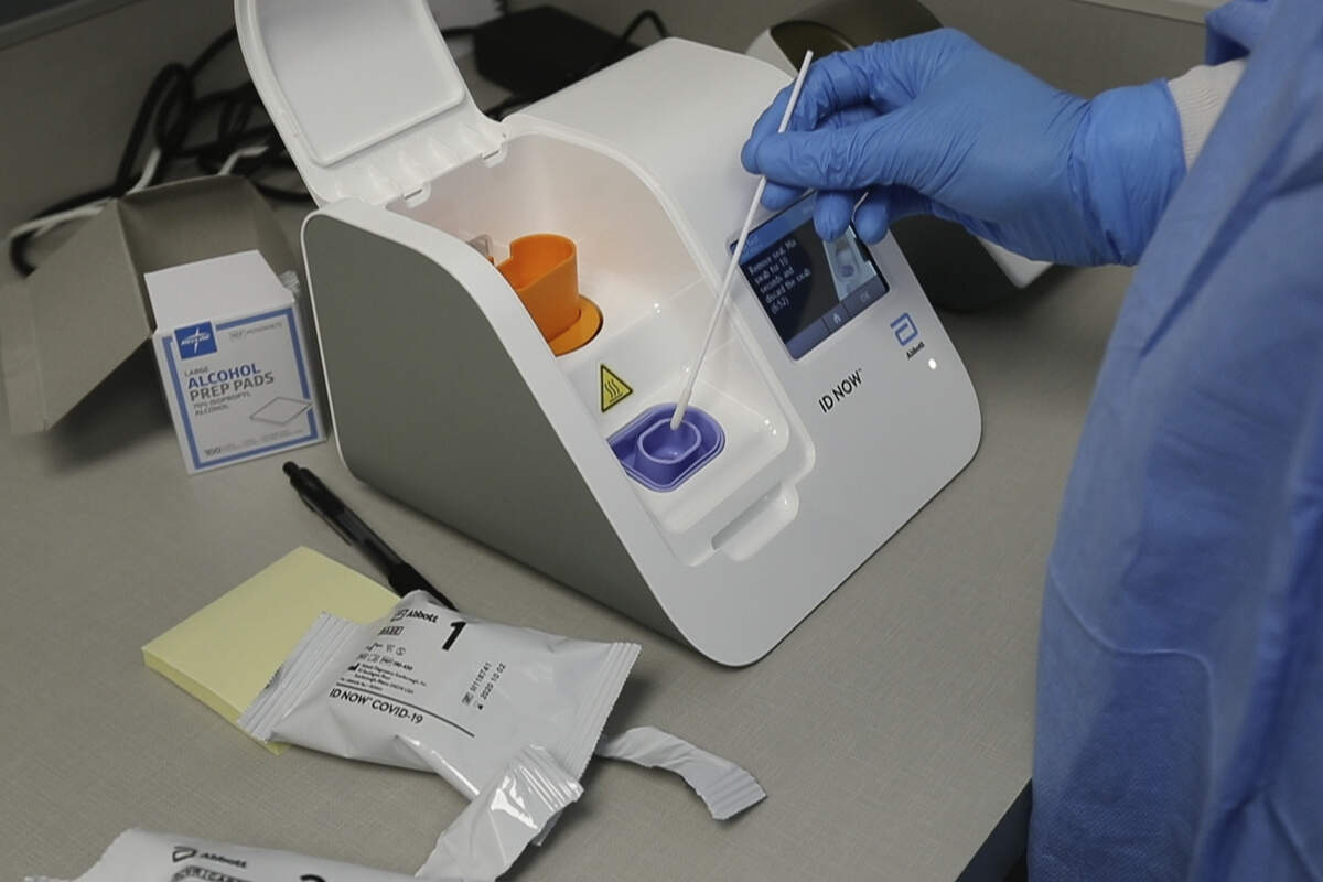 FILE - In this April 10, 2020, file frame grab from video, a lab technician dips a sample into the Abbott Laboratories ID Now testing machine at the Detroit Health Center in Detroit. Illinois-based Abbott Laboratories says its cartridge-based test, approved last month, delivers results within minutes. The coronavirus pandemic gave rise to bold promises by President Donald Trump as he led the response in the U.S. (AP Photo/Carlos Osorio)