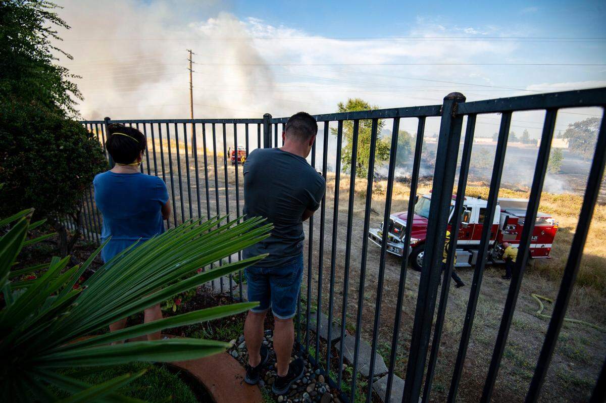 Residents of the Blue Oaks neighborhood in Roseville watch from their yard as members of the Roseville Fire Department and Cal Fire work a grass fire that’s burning in the fields next to their home, Monday, Aug. 10, 2020.