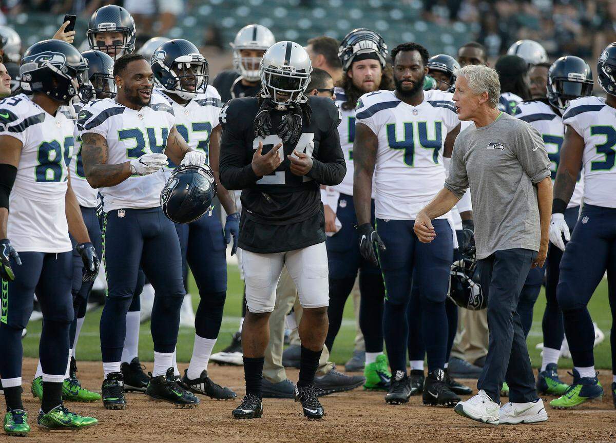 Oakland Raiders running back Marshawn Lynch (24) laughs with Seattle Seahawks head coach Pete Carroll, right, and Seahawks players before a 2017 NFL preseason football game in Oakland.