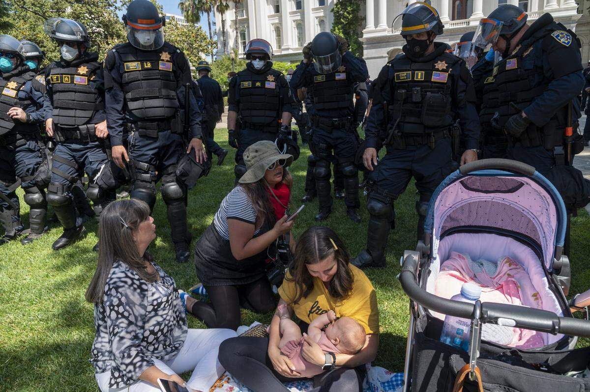 California Highway Patrol officers wait as Amber Beasley breastfeeds her 4-month-old daughter Bailey during a protest on Friday, May 1, 2020, against Gov. Gavin Newsom’s stay-at-home order to slow the spread of the coronavirus. The officers were attempting to clear the Capitol grounds after a dispersal of the crowd was ordered.