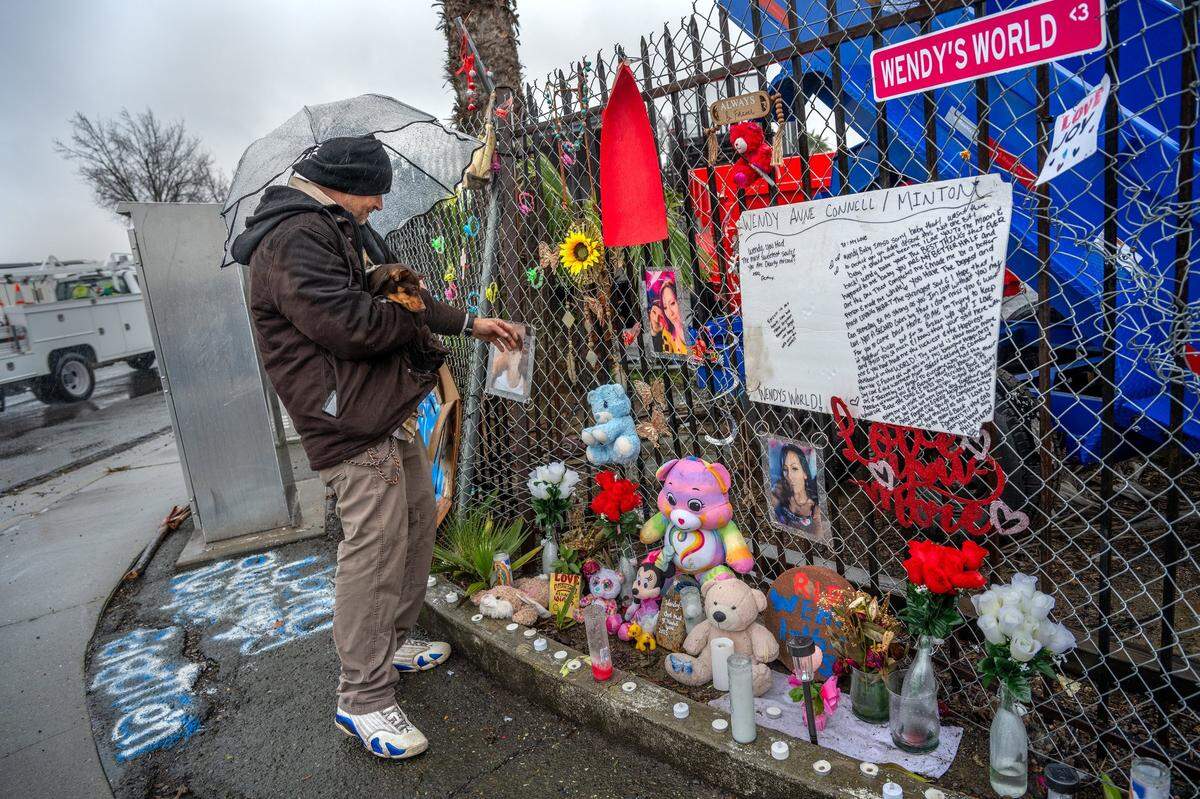 Phillip Minton caresses a photograph of him with his partner Wendy Connell at a memorial for at the intersection of Roseville Road and Longview Drive, a few hundred feet from the homeless shelter where they lived. Connell was fatally struck by a vehicle at the intersection in January. A love letter he wrote to her is attached to the fence at right.
