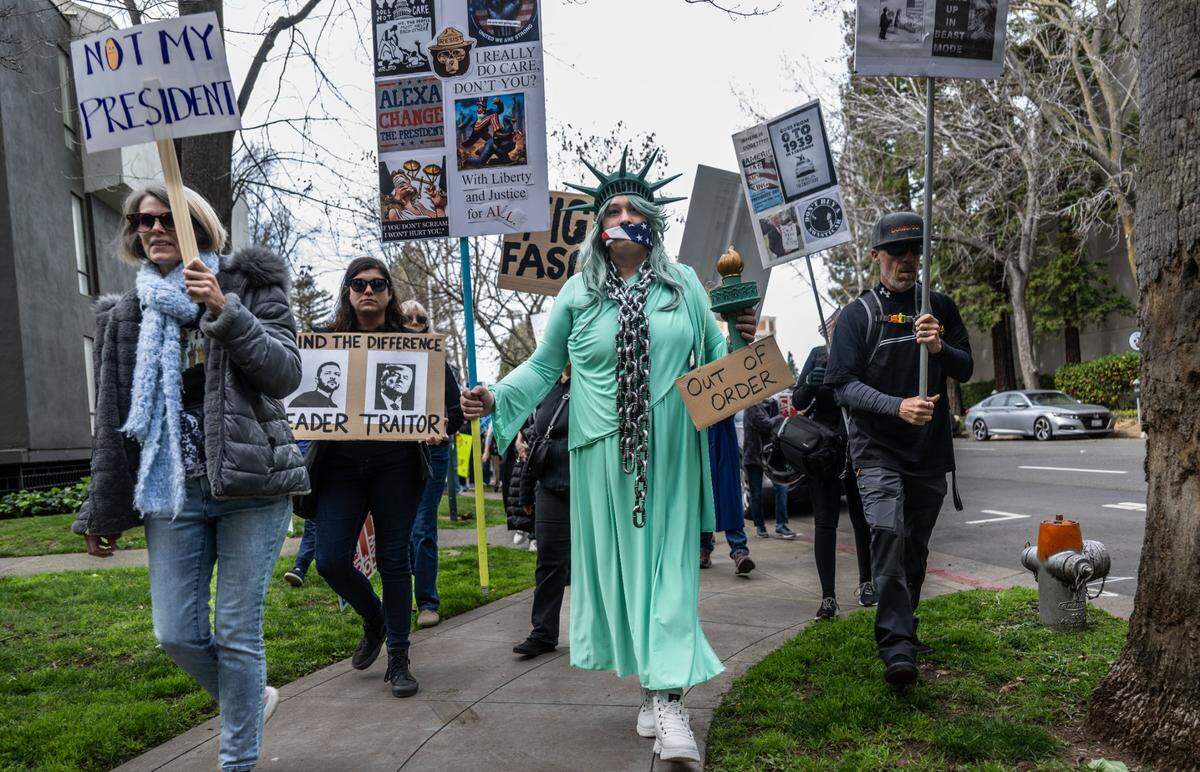 Nicole Ftacnik wears a Lady Liberty costume with a flag around her mouth and a chain on her neck as she participates in the March 4 Democracy against the Trump administration in Sacramento on Tuesday.