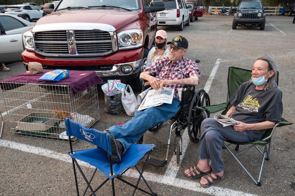 Michael Signor sits with a newspaper on his lap next to his neighbor Maggie Spalding, right, and his daughter Jessica Signor and her 21-year-old cat, at an evacuation center on Missouri Flat Road in Placerville on Wednesday, Aug. 18, 2021. Signor has lived in Pollock Pines for 50 years and was evacuated during the Caldor Fire after a sheriff’s deputy knocked on their door and told them they needed to leave.