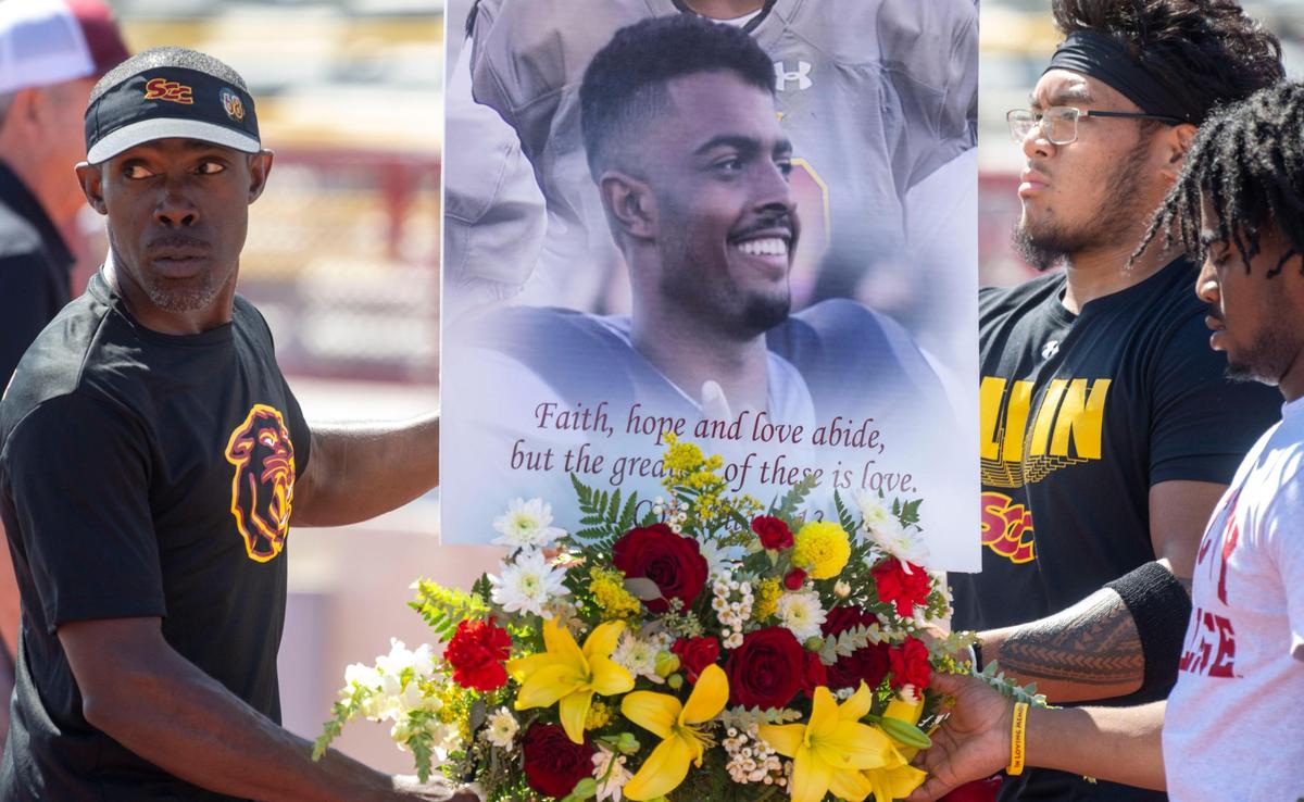 Sacramento City College head football coach Dannie Walker, left, brings a photo and flowers to the field before the start of their game Saturday, Sept. 16, 2023, in honor of 19-year-old offensive tackle Justin McAllister who died on Sept. 11, 2023, during practice.