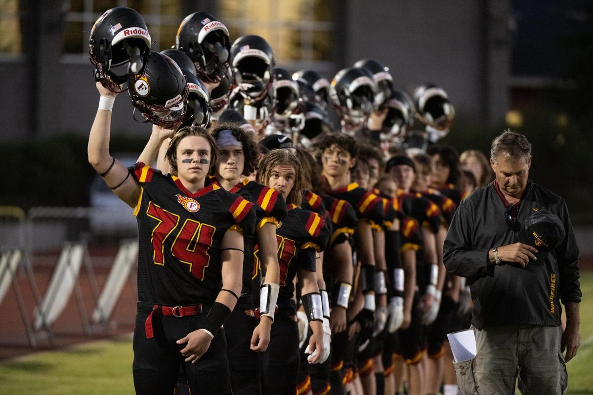 Jordan Overstreet (74) and the Foresthill Wildfires raise their helmets during the National anthem before the game against Valley Christian Lions at Foresthill High School in Foresthill on Friday. It was their first home game since the Mosquito Fire.