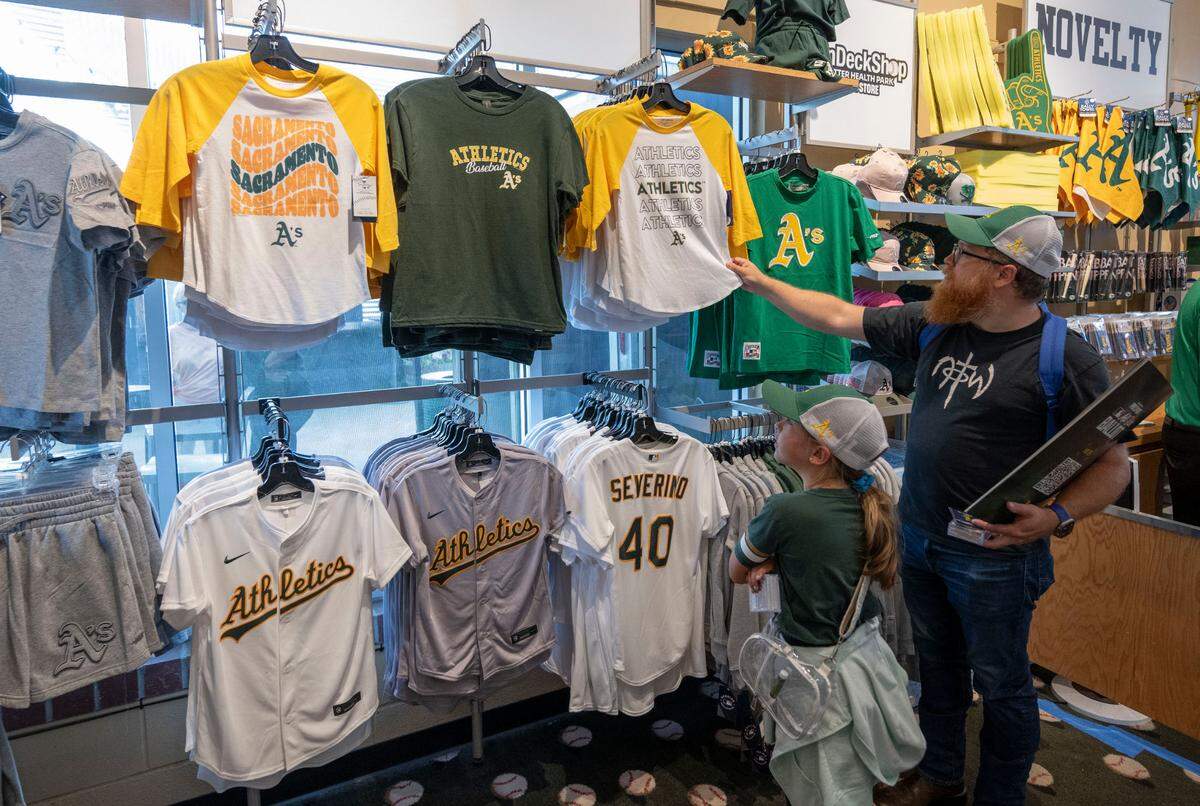 Stephen Washburn of Elk Grove and his 9-year-old daughter Norah look at some of the merchandise at the Athletics team store before a MLB game at Sutter Health Park on Friday.