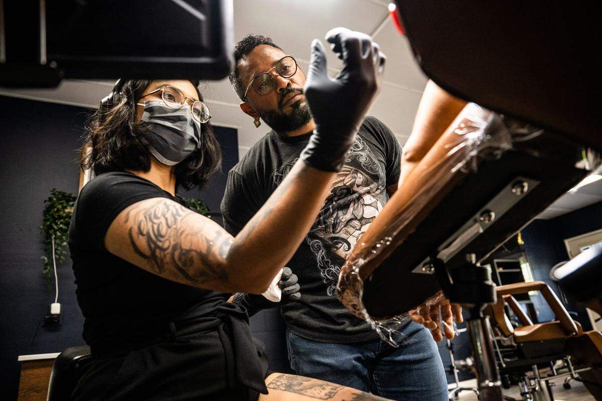 David Ramses Cabral, co-owner of Ghost Ink tattoo studio in Sacramento, talks with artist Jo Mean as they discuss how to better position herself as she works on a tattoo Tuesday.