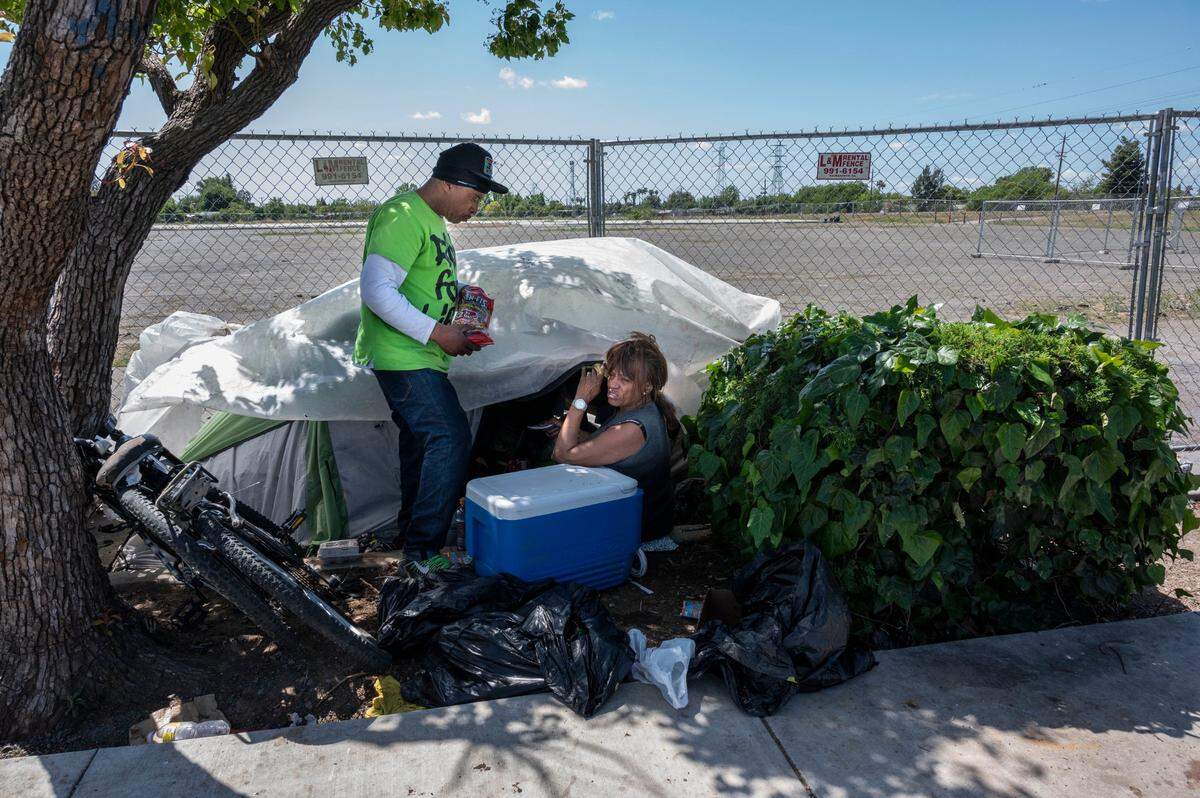 Unhoused residents Antoine Williams, of West Sacramento, and Belinda Stewart, of south Sacramento, visit the tent of a friend April 20, near a vacant lot on Florin Road planned to be Sacramento County’s first “Safe Stay Community.” Neighbors on Florin Road oppose the plan, saying the village should go somewhere else.