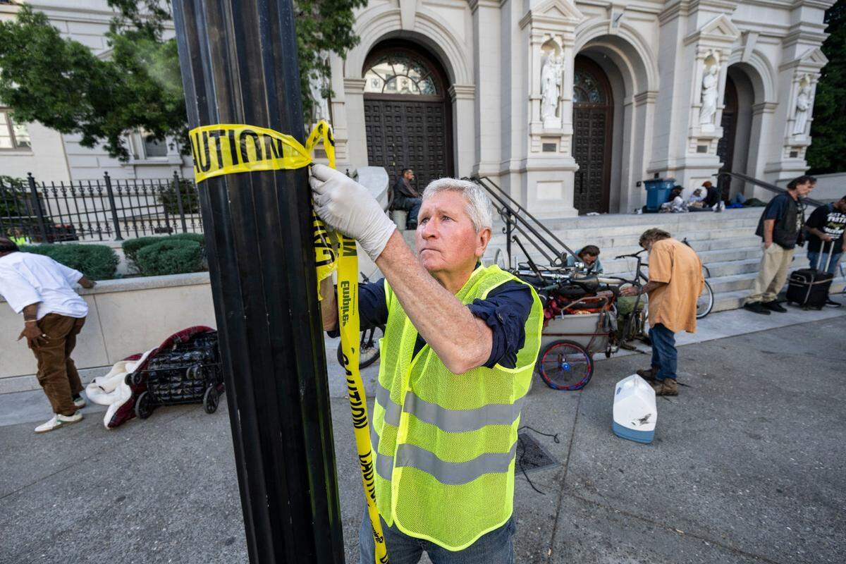 Bill Feller, a volunteer with the Brown Bag Lunch at the Cathedral of the Blessed Sacrament, helps put up caution tape for a food line on Thursday.